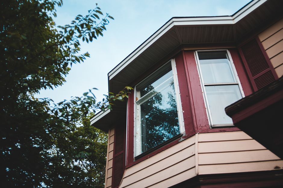 A cottage facade with windows reflecting trees and sky.