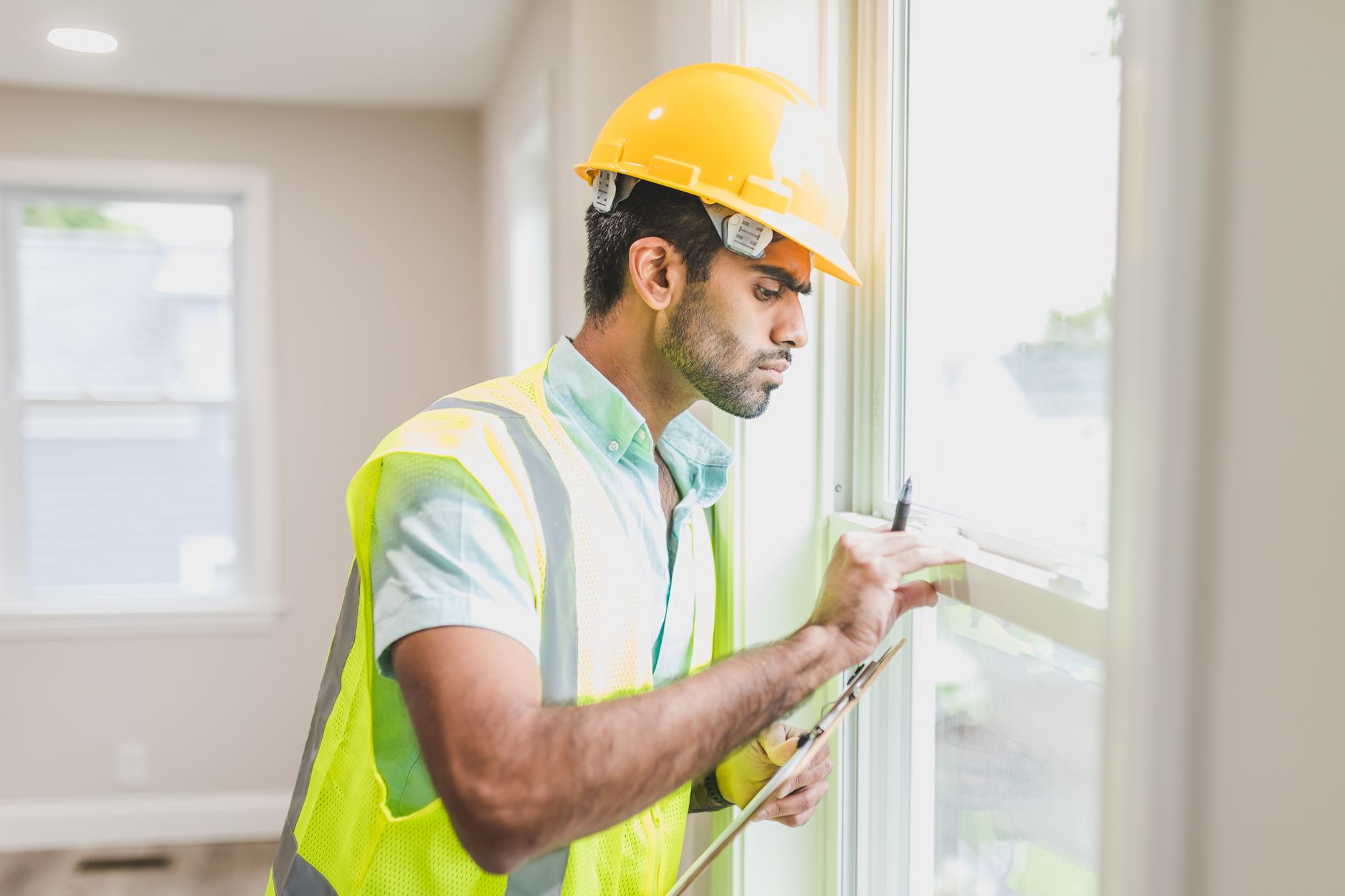 Construction worker with hard hat and vest inspecting window indoors, side view in Austin, TX